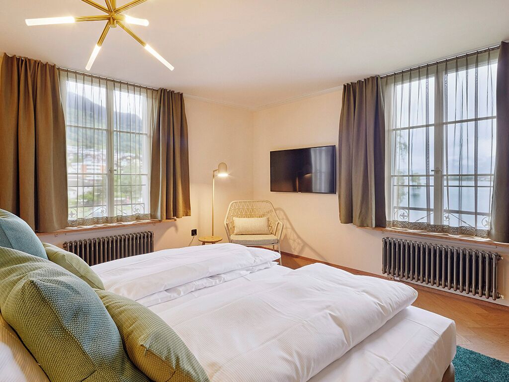 Una habitación de hotel con cama, sillón, televisión y ventanas amplias.