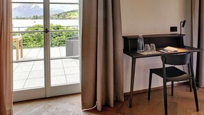 Habitación moderna con escritorio, silla y vistas a un lago y montañas a través de una puerta de cristal.