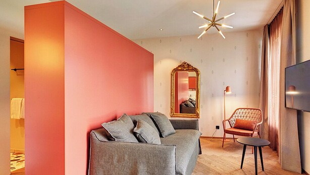 Una sala de estar moderna con un sofá gris, una pared de acento roja, un espejo grande, un televisor y una silla geométrica original.