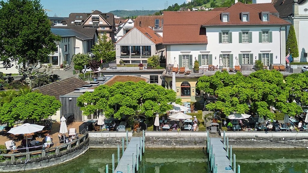 Vista al río con un muelle, edificios y zonas de estar al aire libre.