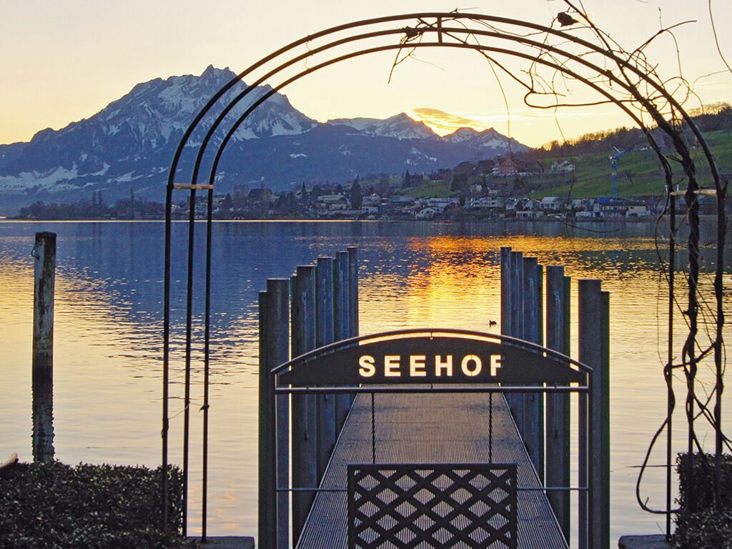 A metal gate with the inscription "SEEHOF" in front of a lake with mountains in the background.