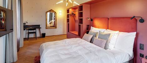 A modern bedroom with a large bed, a desk, and a mirror.