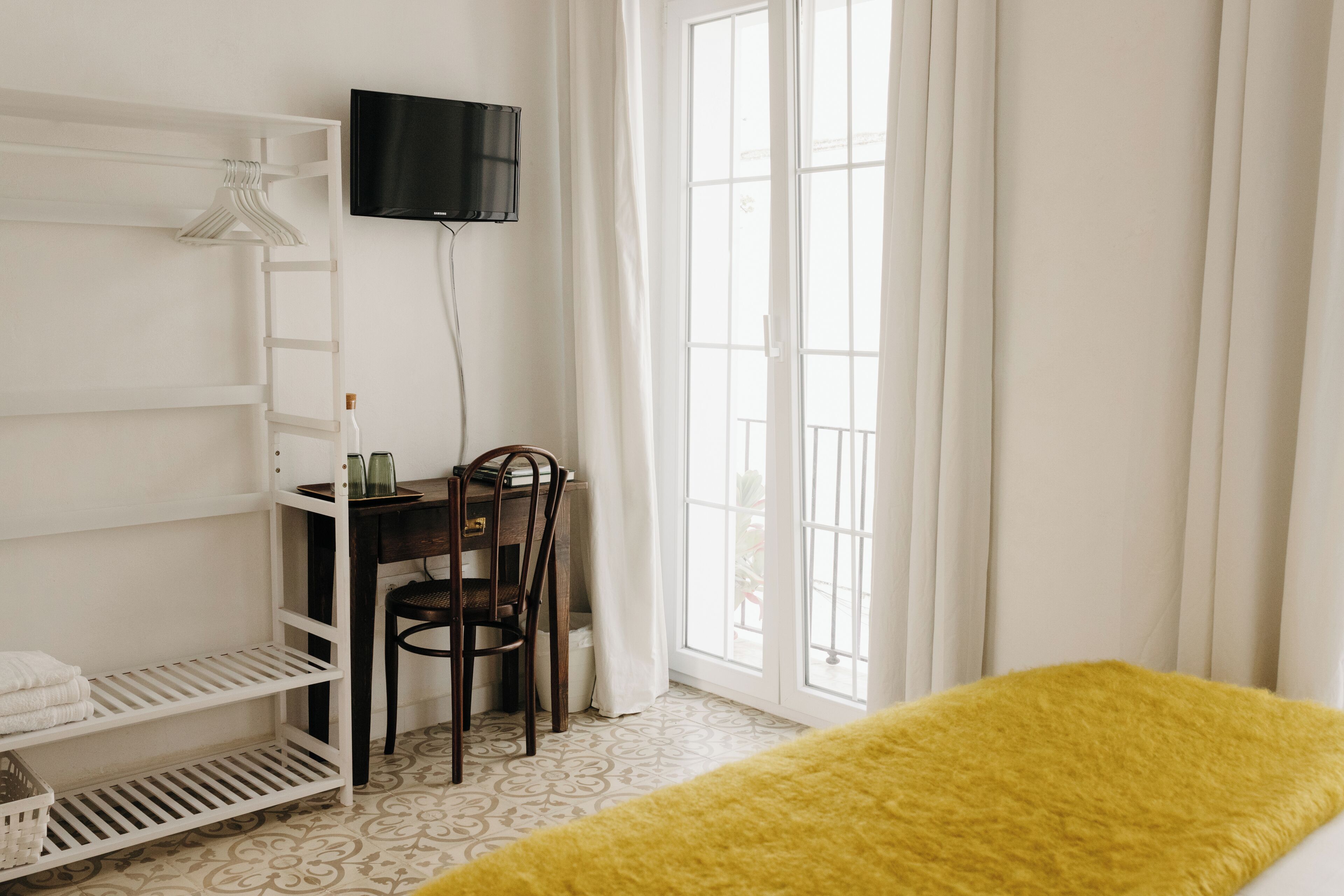 Ein Zimmer mit einem Bett, einem Schreibtisch mit Stuhl, einem an der Wand befestigten Fernseher und einem Fenster mit Vorhängen.