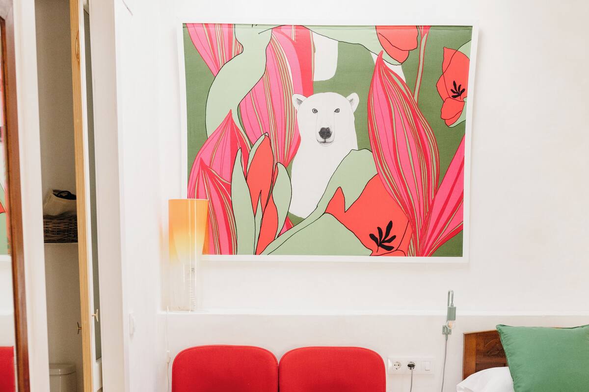 A small, cozy room with a red chair, a small table, and a bed with a green pillow.