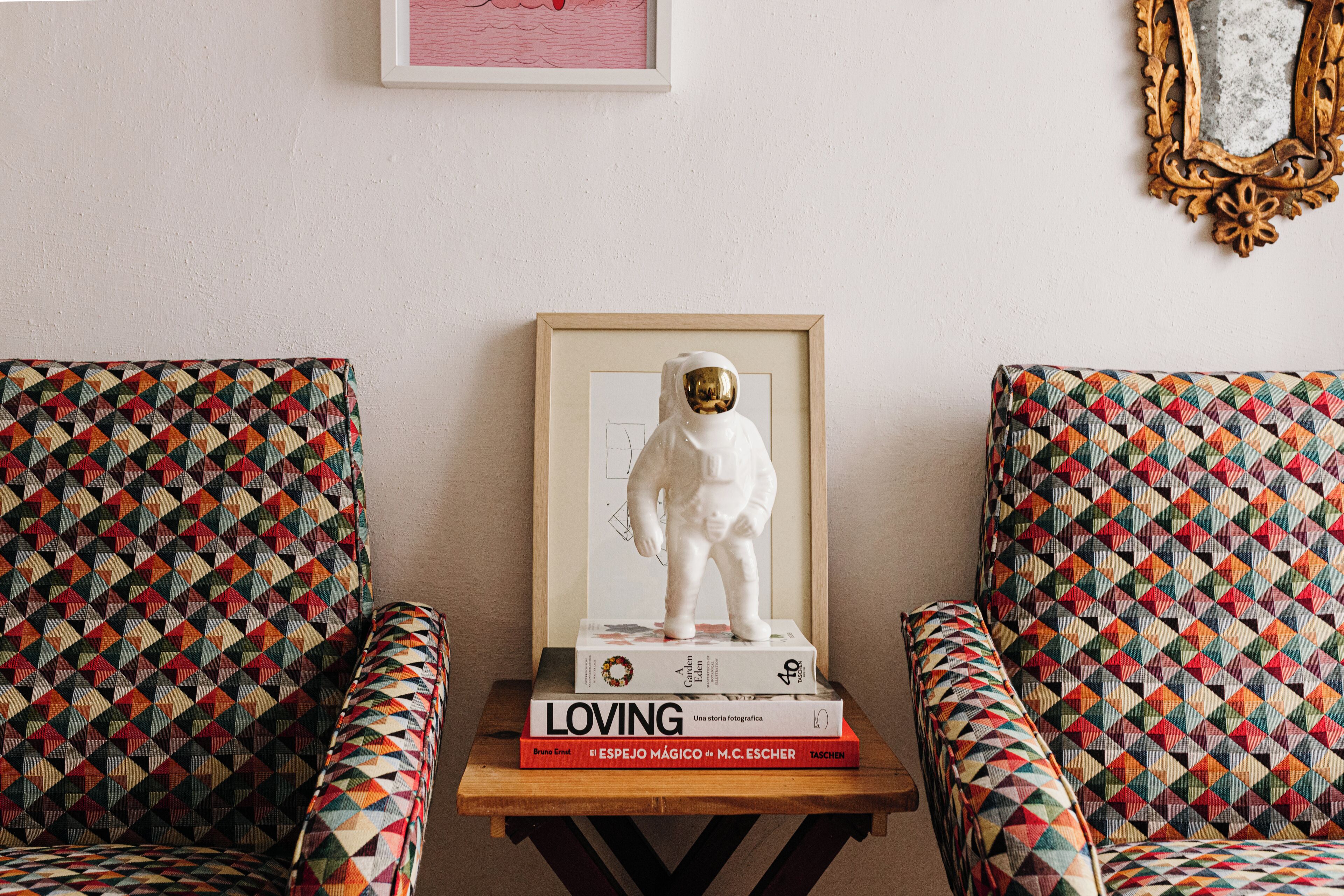A room with two patterned armchairs, a small table with a framed sculpture, and a few books.