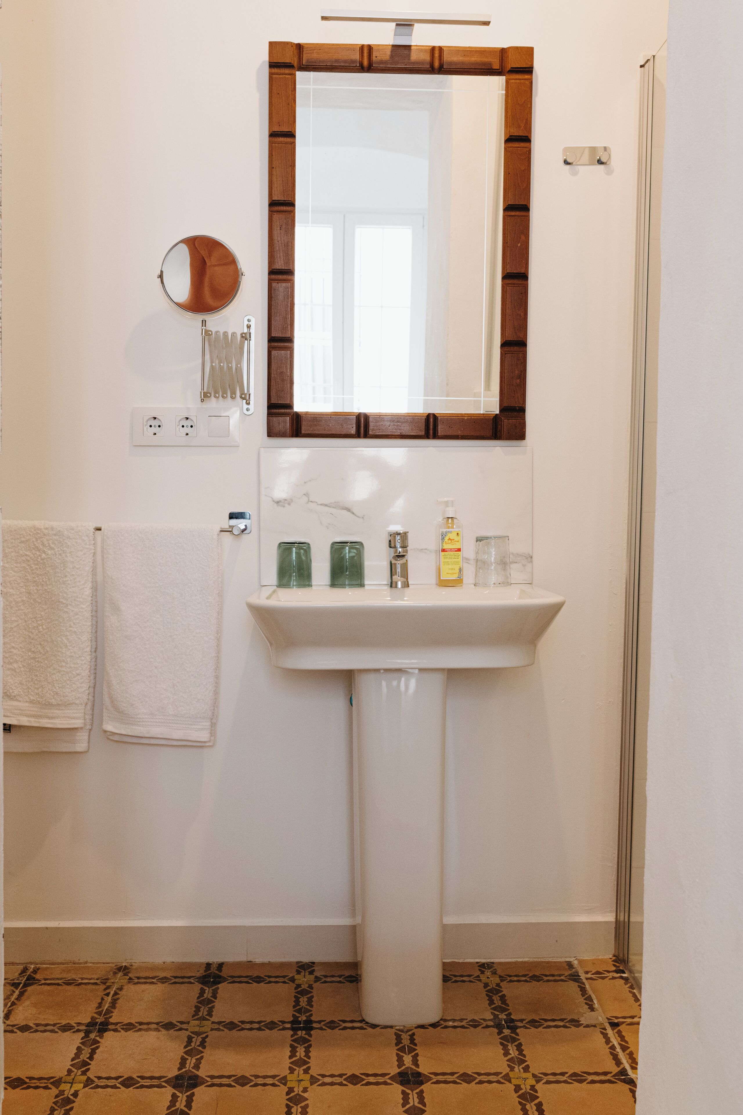 Un baño con un lavamanos blanco, un espejo y un perchero para toallas.
