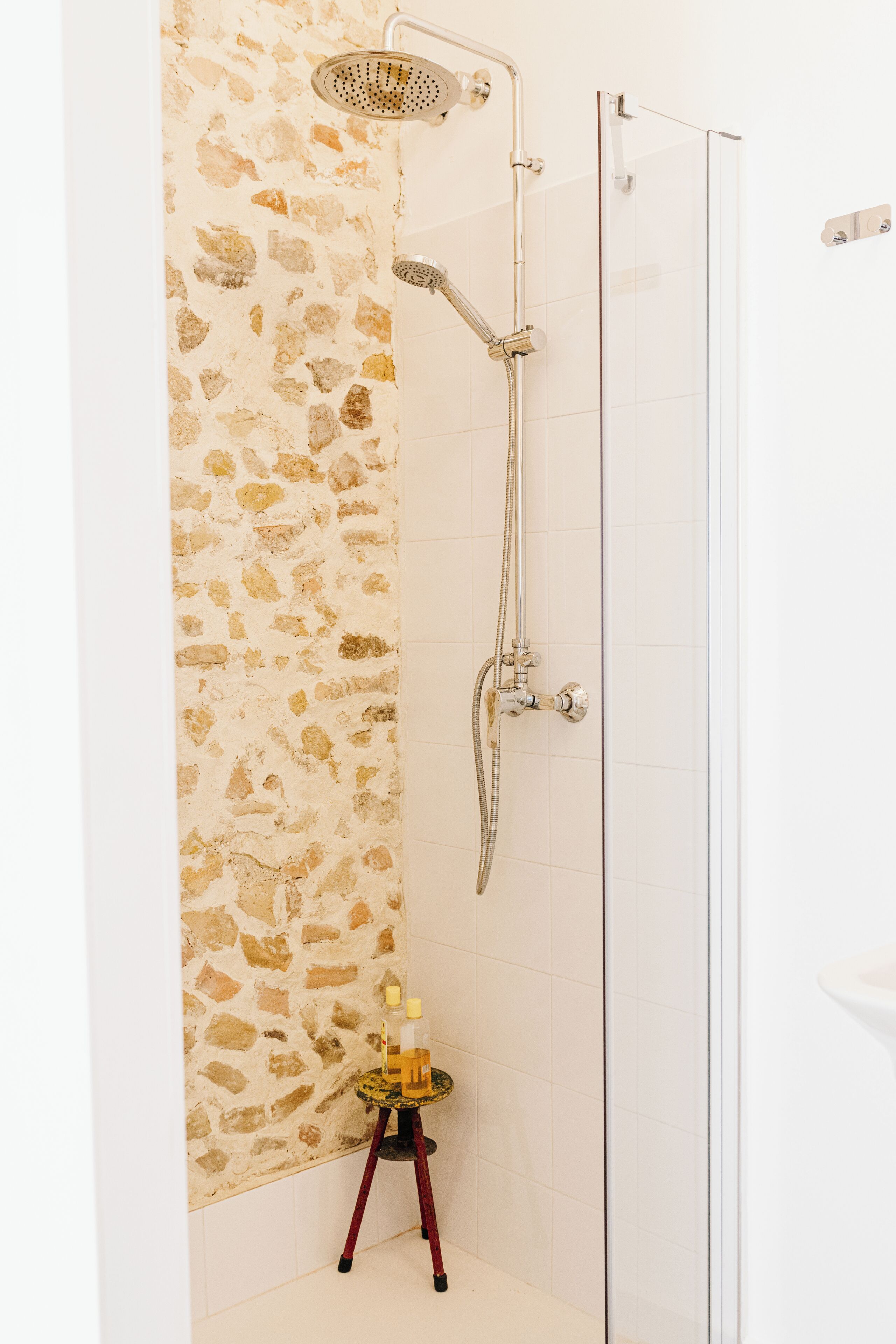 A shower with a stone wall, a glass door, and a small table with toiletries.