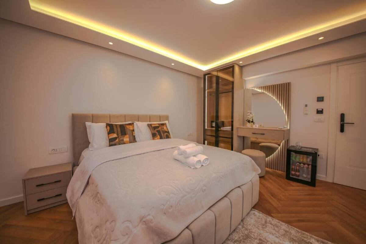 A modern bedroom with a large bed, bedside tables, a vanity, and a walk-in closet.