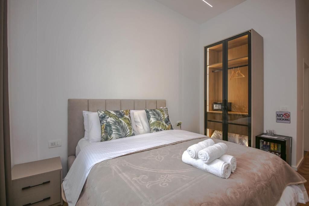 Una habitación de hotel con una cama, un armario, un letrero de 'No Fumar' y una mesita de noche con lámpara.