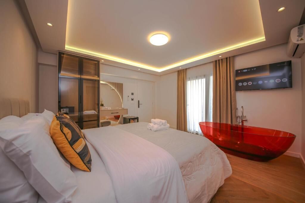 A modern hotel room with a large bed, a red bathtub, a TV, and a desk with a chair.