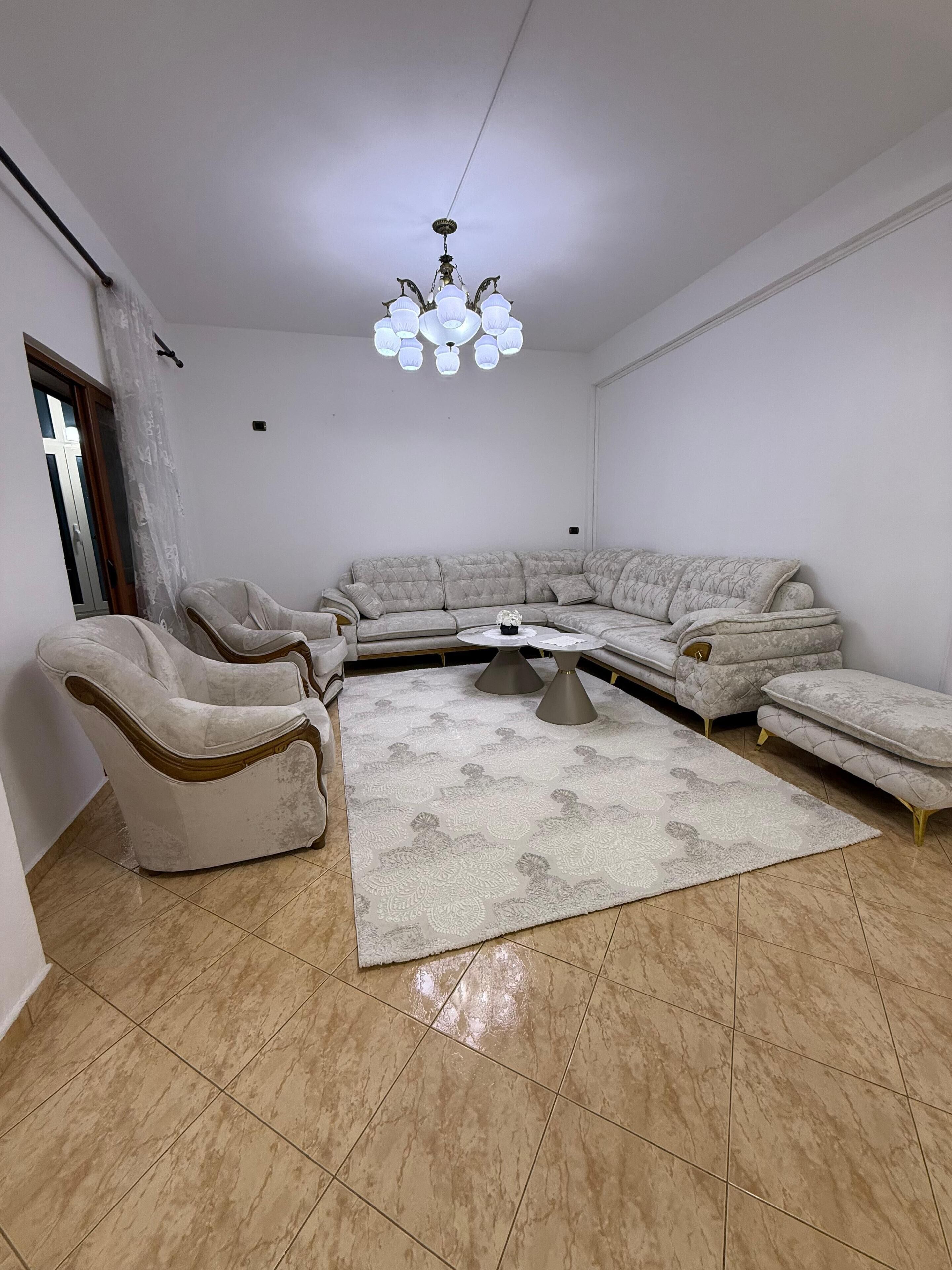 A living room with a sectional sofa, two armchairs, a coffee table, and a chandelier.