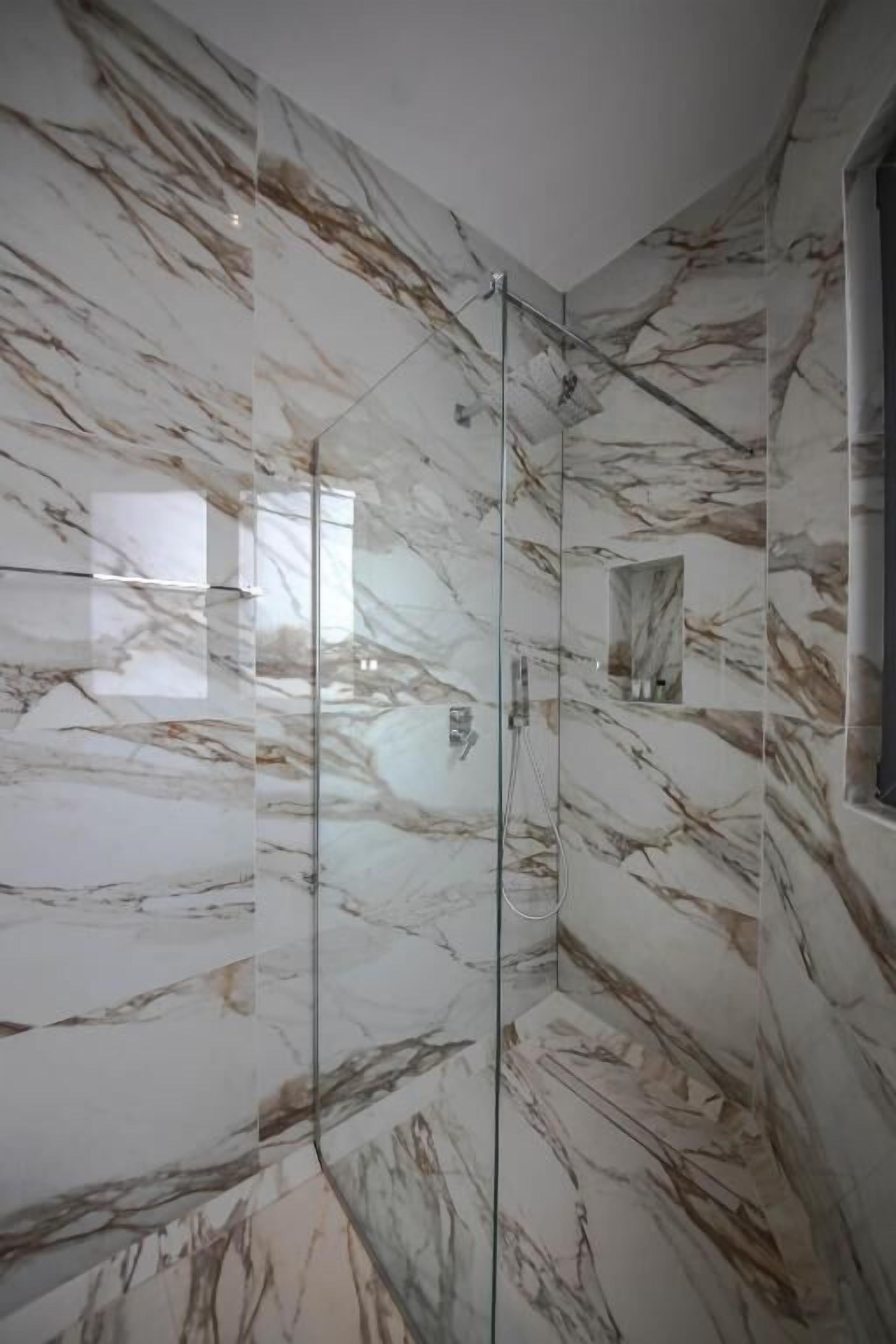 A modern bathroom with marble walls and a glass shower enclosure.