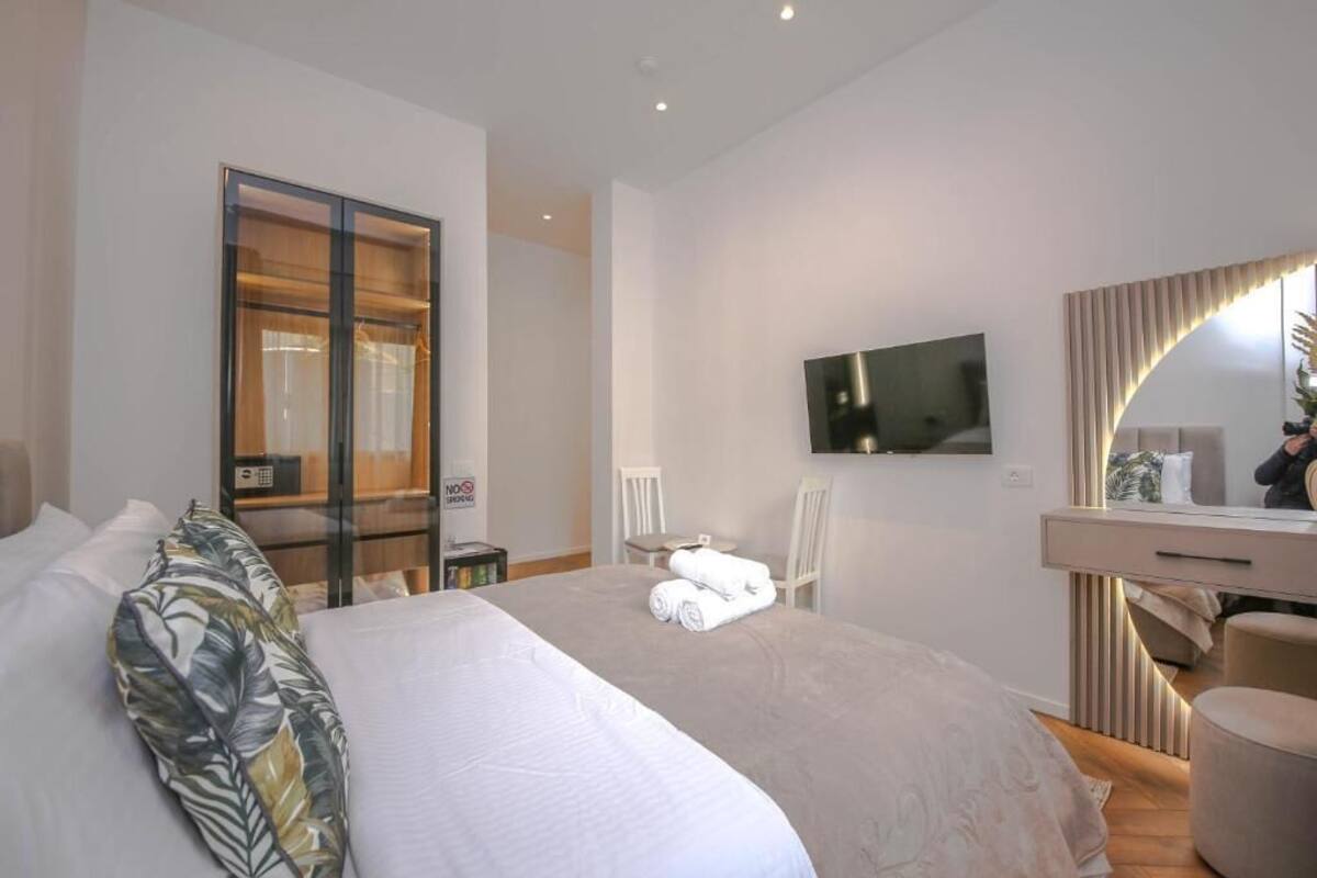 A hotel room with a bed, a TV, a desk with a mirror, and a chair.