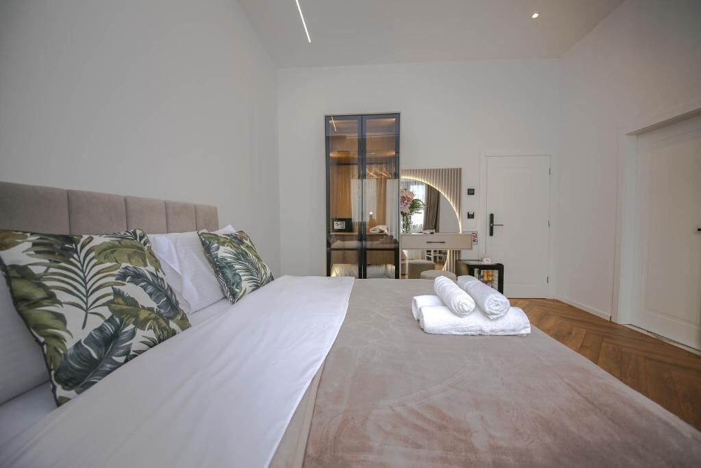 A modern hotel room with a large bed, a mirror, and a small table with towels.