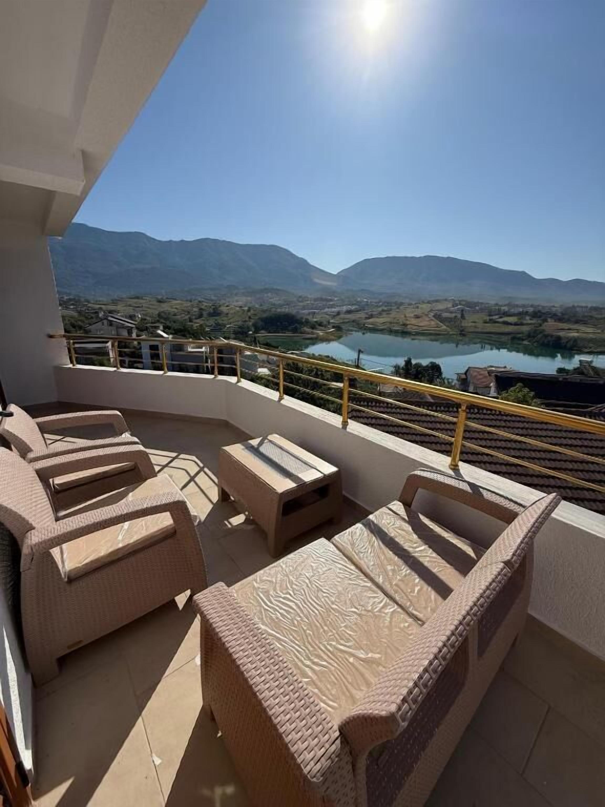 A balcony with wicker furniture, a view of mountains, and a lake.