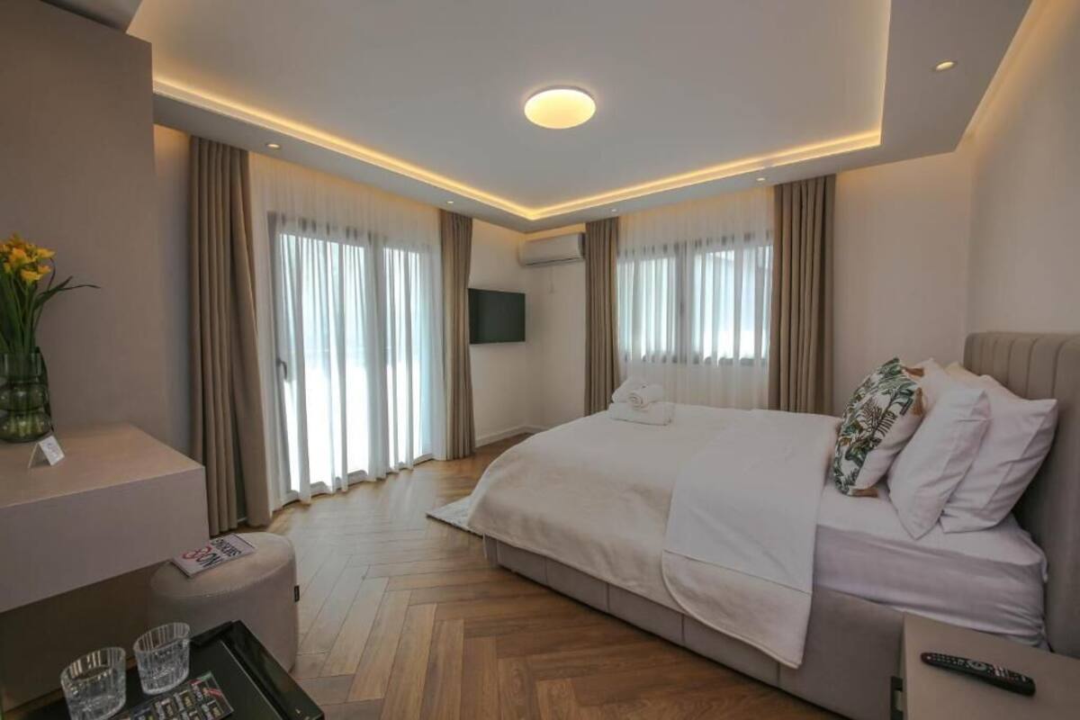 A modern hotel room with a large bed, a flat-screen TV, a bedside table, and a small desk with a chair.
