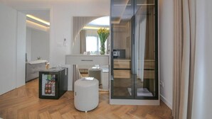 A modern hotel room with a glass partition, a minibar, a seating area, and a view of the outdoors. - Murati Lake View Hotel (Farkë)
