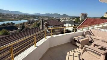 Un balcón con vista a un lago y montañas, muebles de exterior y suelo de baldosas.