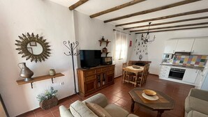 Un salon comprenant un canapé, un téléviseur, une table à manger avec des chaises, une cuisine équipée et un mur décoratif.