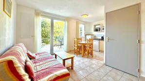 A cozy living room with a sofa, a small table, and a kitchen area with a fridge, microwave, and a dining table with chairs. - Terrasse du Sud, 4 guests, Pool in Calvisson (Calvisson)