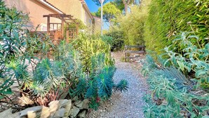 A garden with a gravel path, various plants, a wooden pergola, and a building with a tiled roof. - Le Soleil du Mas, 2 guests, Pool in Calvisson (Calvisson)