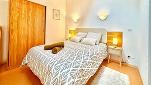 A bedroom with a bed, wooden ceiling beams, a nightstand, and wall-mounted lights. - Le Soleil du Mas, 2 guests, Pool in Calvisson (Calvisson)