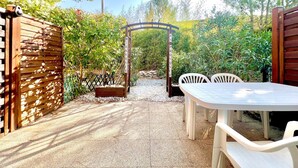 An outdoor patio area with a wooden pergola, a table with chairs, and a gravel path leading to a gate. - Le Soleil du Mas, 2 guests, Pool in Calvisson (Calvisson)