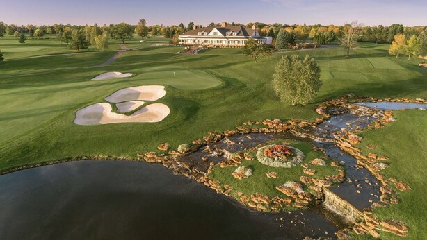 A golf course with bunkers, a pond, and a large building in the background. - The Crescent (Verona)