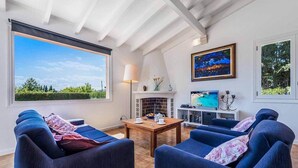 A spacious living room with a high ceiling, large windows, a fireplace, and a television. - Villa Patricia (Pollença)