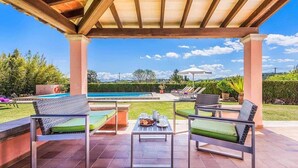 An outdoor patio with two lounge chairs, a table, and a view of a swimming pool and garden. - Villa Patricia (Pollença)