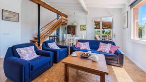 A spacious living area with blue sofas, a wooden coffee table, and a staircase leading to an upper floor. - Villa Patricia (Pollença)