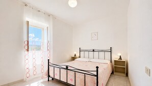 Quarto com cama, duas mesas de cabeceira, janela com cortinas e luminária na parede.