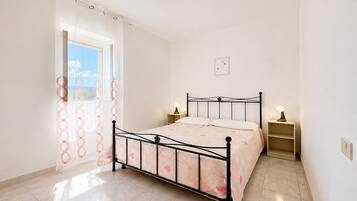Un dormitorio con una cama, dos mesitas de noche, una ventana con cortinas e iluminación en la pared.