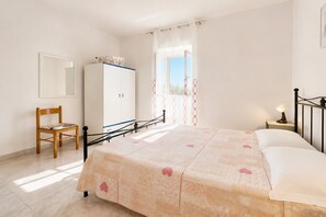 A bedroom with a bed, a wooden chair, a wardrobe, a window with curtains, and a nightstand with a lamp.