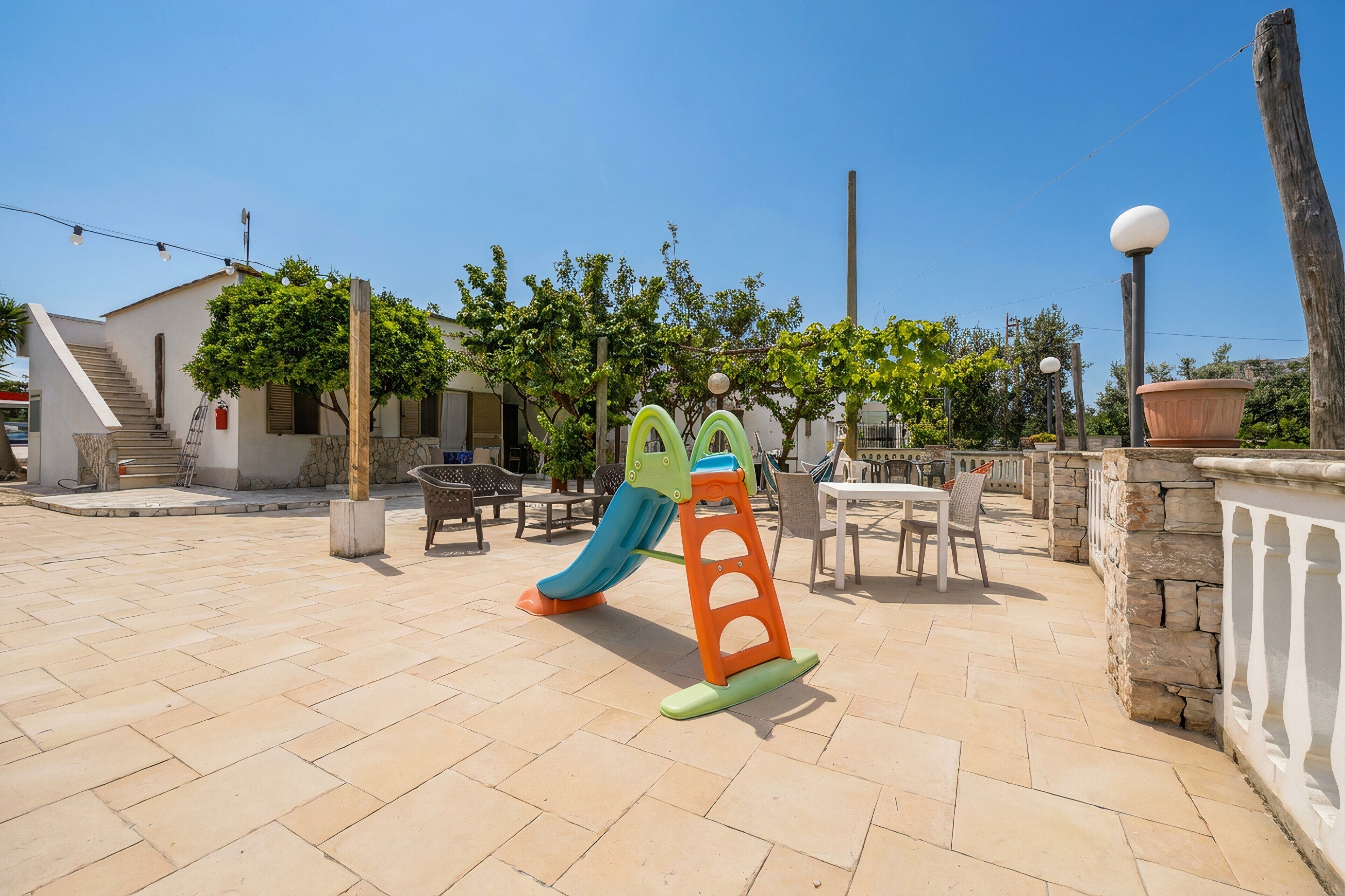 Un parque infantil con tobogán y estructura para escalar, mobiliario exterior y un edificio con escaleras.