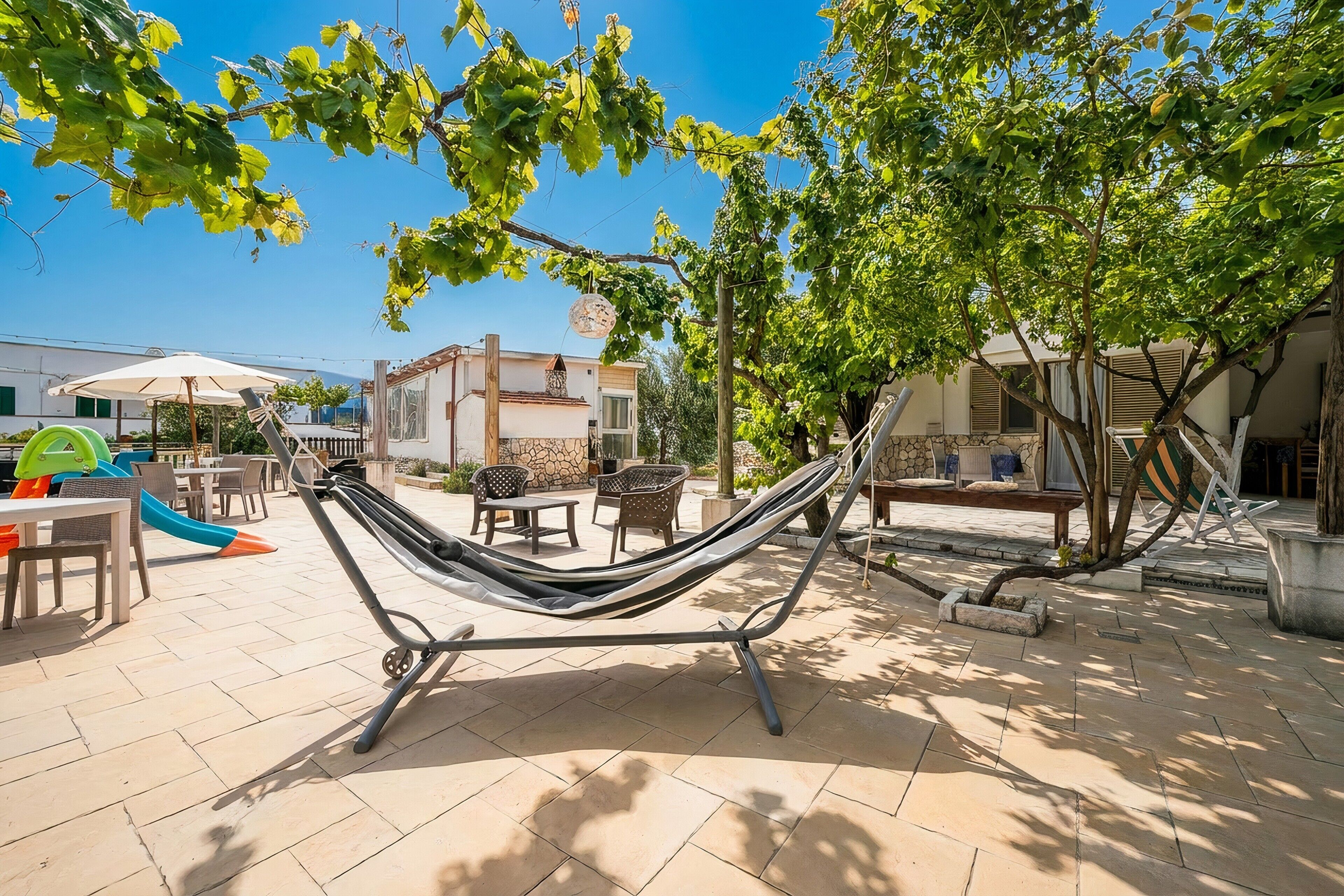 Una hamaca en un patio con muebles de exterior, una estructura de juegos y un edificio al fondo.