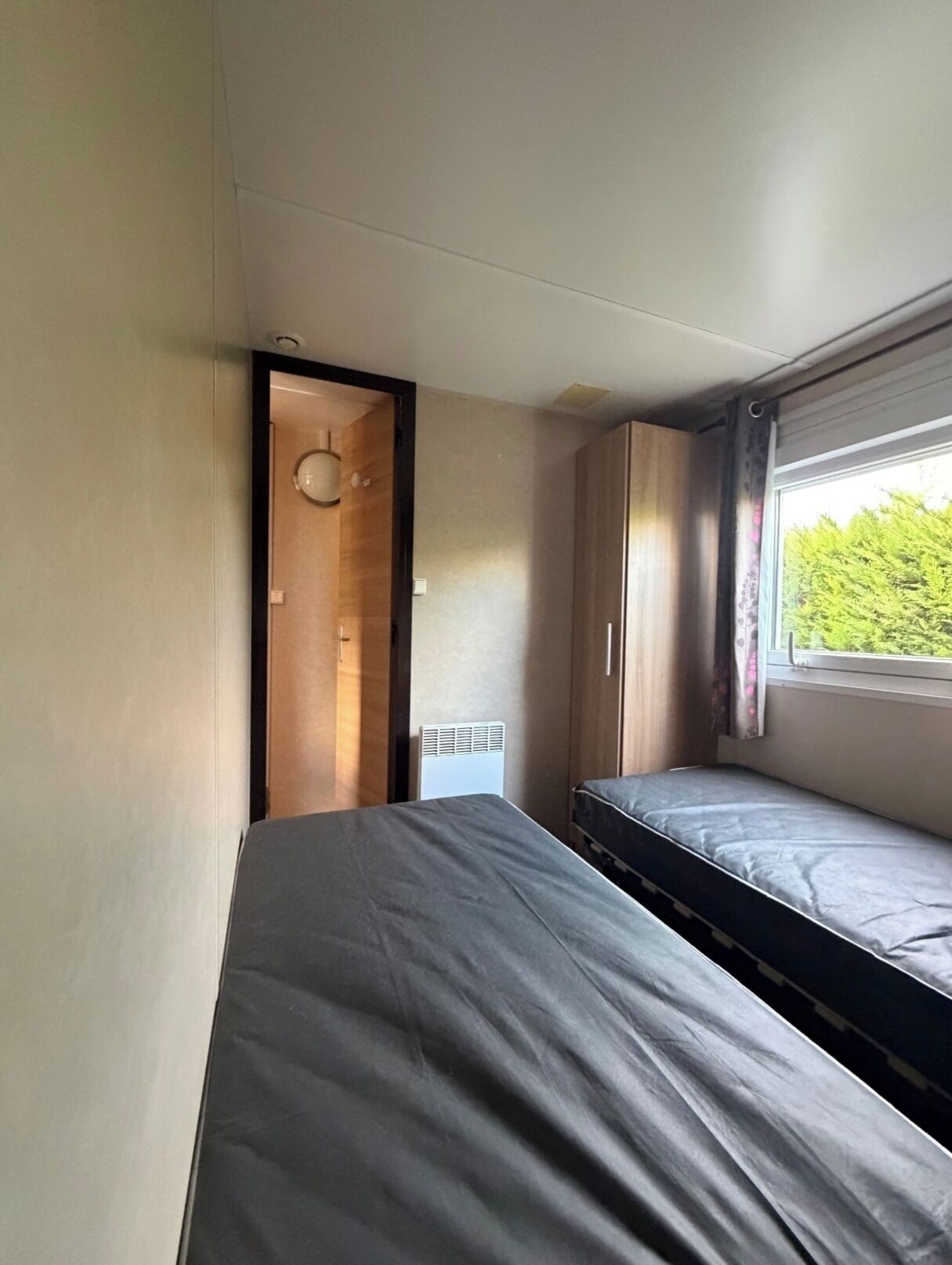A compact room with two beds, a radiator, and a window with curtains.