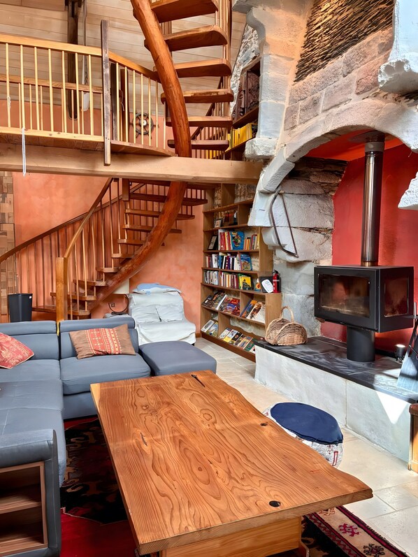 A cozy interior with a wooden staircase, a sofa, a table, a bookshelf, and a fireplace.