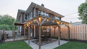 A covered patio area with a wooden pergola and string lights, a dining table, and a barbecue grill. - LOCATION! 3BR Near UNMC, Creighton, UNO & Downtown (Omaha)
