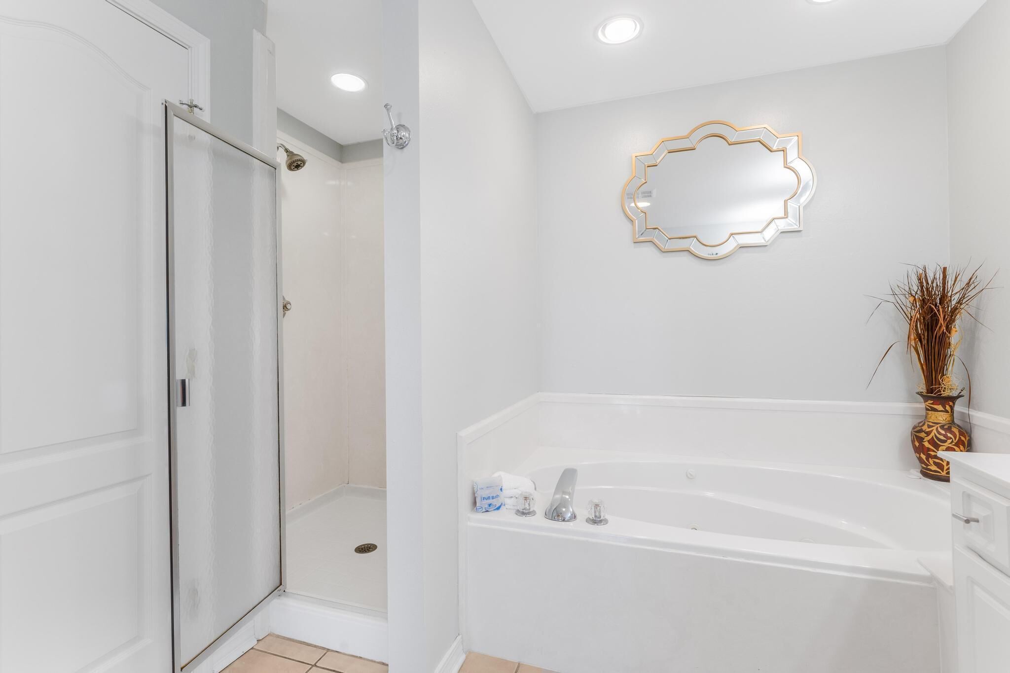 A bathroom with a glass shower enclosure, a white bathtub, and a decorative mirror on the wall.