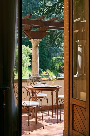 A patio with a table and chairs, a decorative metal structure, and a view of greenery.
