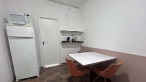 Ein kleines Zimmer mit einem weißen Kühlschrank, einer Mikrowelle, einer Kaffeemaschine und einem Tisch mit zwei Stühlen.
