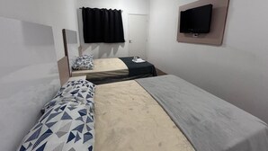 Ein schlichter, kleiner Raum mit zwei Einzelbetten, einem flachbildfernseher an der Wand und einem Deckenventilator.