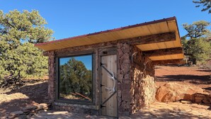 A stone building with a large window and a wooden door, surrounded by a stone patio and trees.