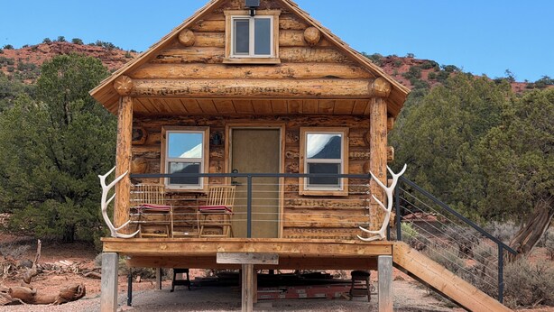 A wooden cabin with a porch, two windows, and a door.