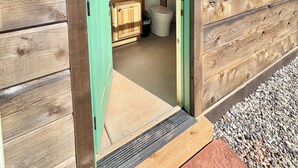 A wooden cabin with a green door leading to a bathroom that includes a toilet and sink.