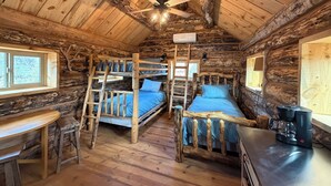 A rustic cabin with two bunk beds, a wooden desk, a coffee maker, and a ceiling fan.