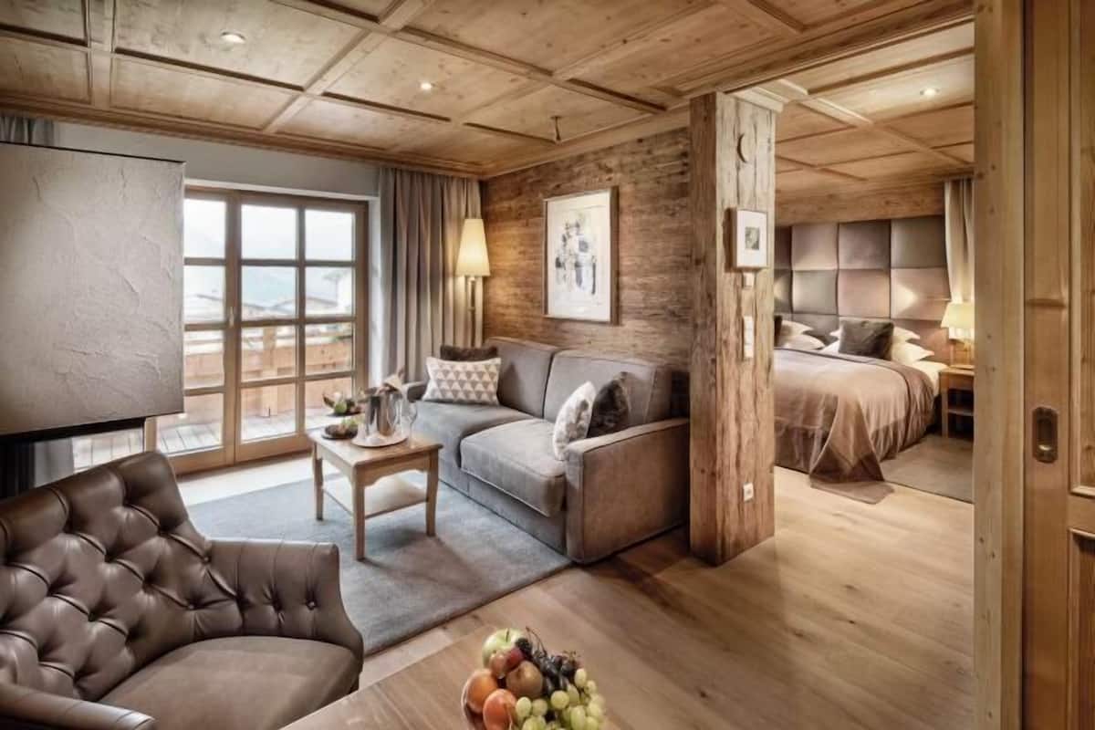 Ein gemütliches Zimmer mit einer Couch, einem Sessel, einem kleinen Tisch mit einer Lampe und einem Bett mit Kopfteil.