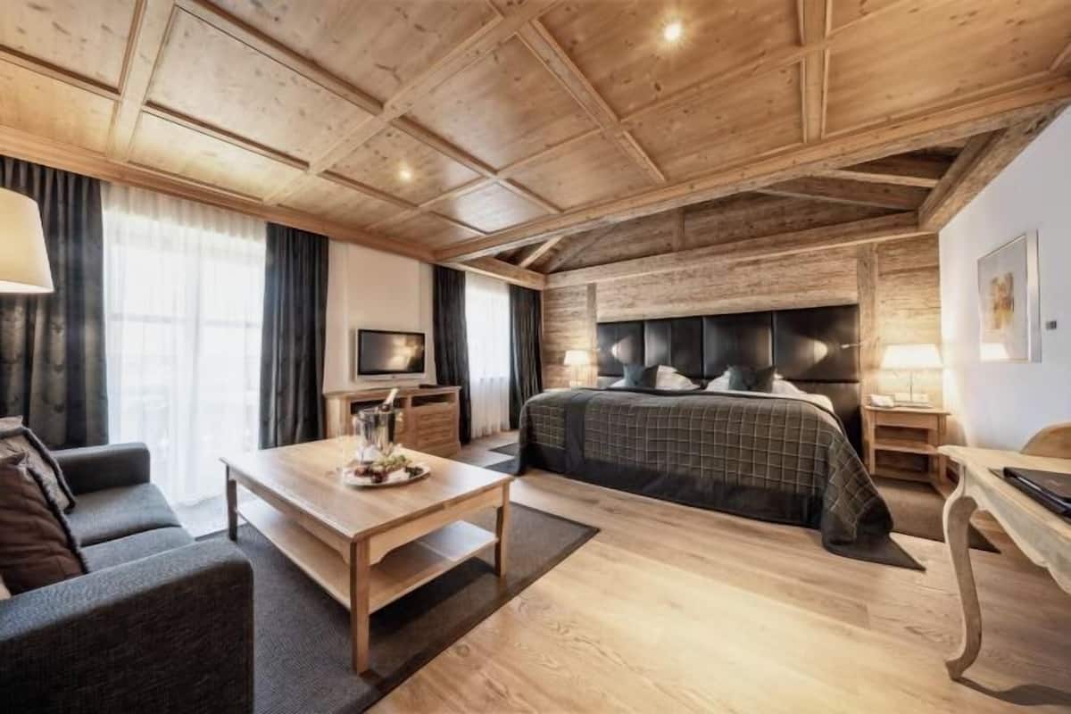 Ein modernes Hotelzimmer mit Holzboden, einem großen Bett mit Kopfteil, einer Couch, einem kleinen Tisch und einem Fernseher.