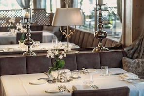 Un espace repas avec des tables mises pour le service, agrémenté d’un vase de fleurs, d’une lampe et offrant une vue par la fenêtre.